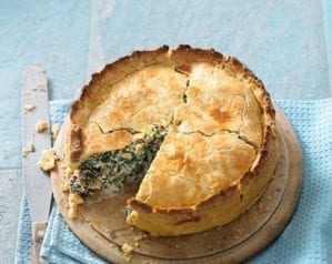 A raised pie with a slice cut out to show the green ingredients inside