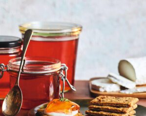 Three jars of wine jelly, with some spooned onto a cracker with goat's cheese in the foreground